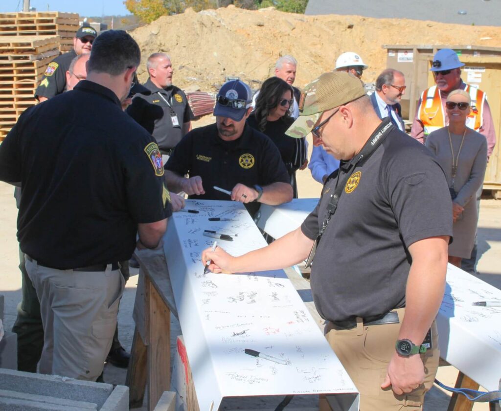 Group of officials signing steel beam at construction site ceremony.