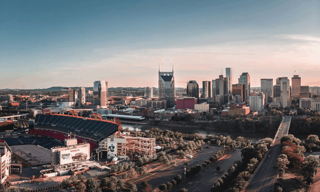 Aerial view of downtown Nashville skyline with stadium and river during sunset.