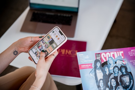 Person scrolls social media in front of laptop with magazine in frame